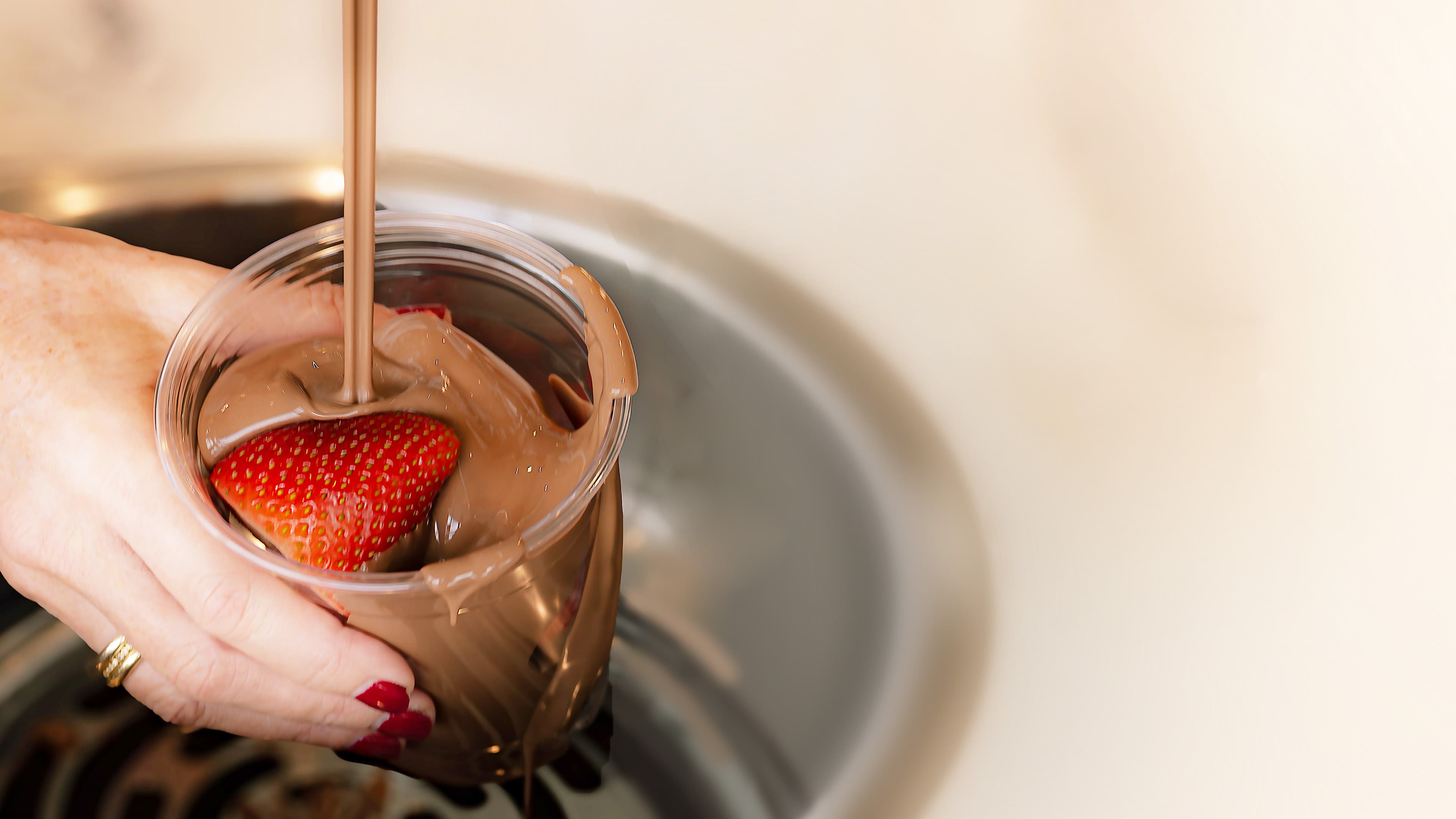 A strawberry being dipped into warm Swiss chocolate